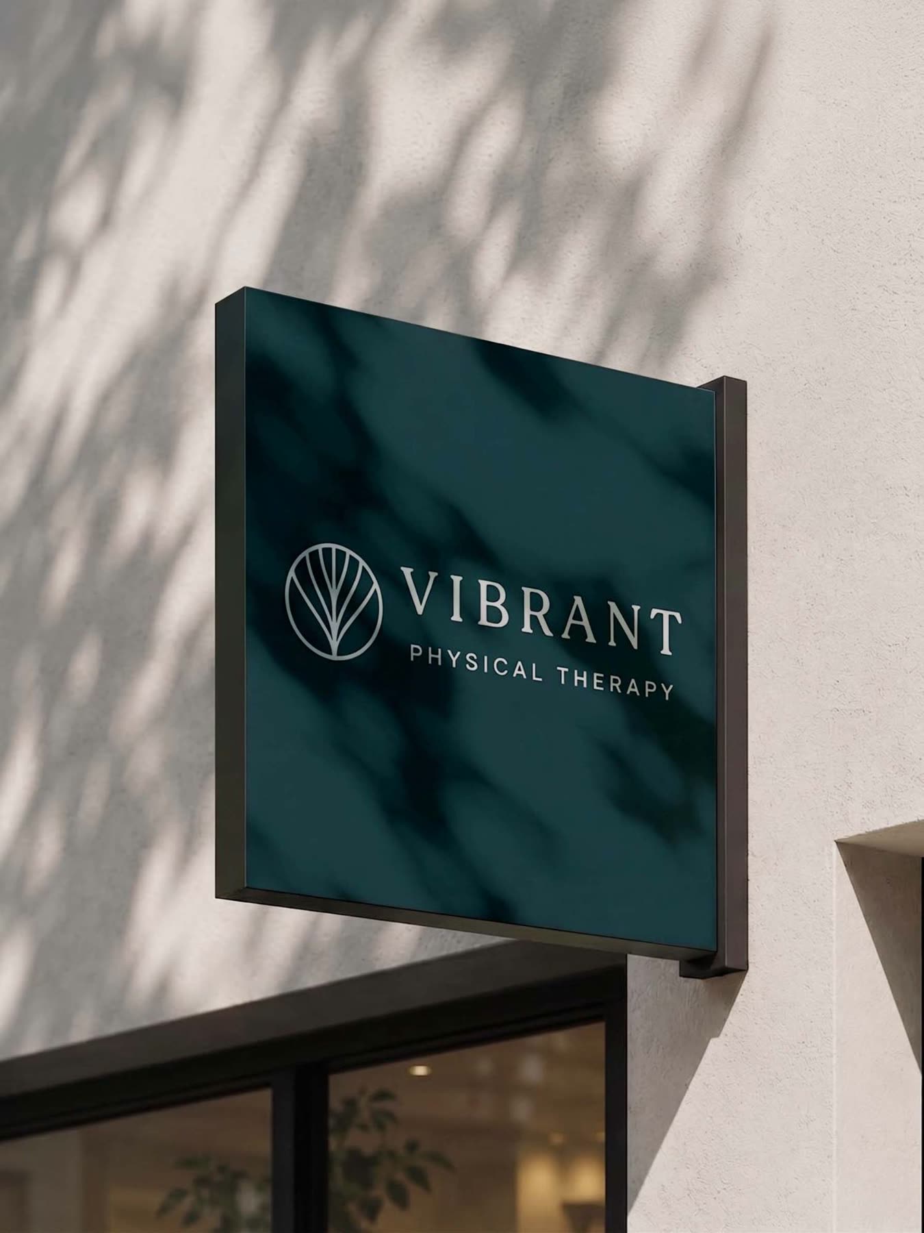 Deep teal hanging sign with the Vibrant Physical Therapy logo, dappled with leaf shadows